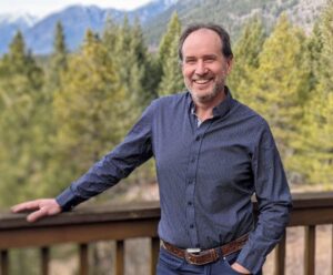 Duncan Cryle smiling on a wooden deck at Clear Sky Centre with a scenic mountain forest backdrop on a sunny day