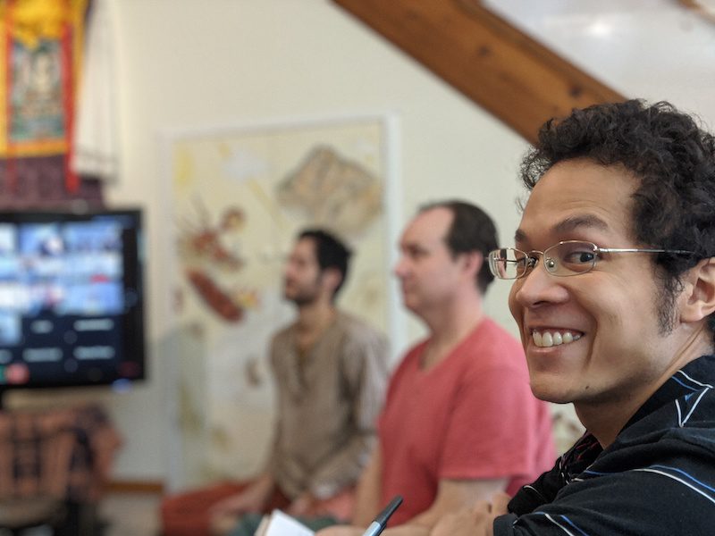 Joyful man in glasses during a virtual meditation session with a group participating in a lively video call discussion.